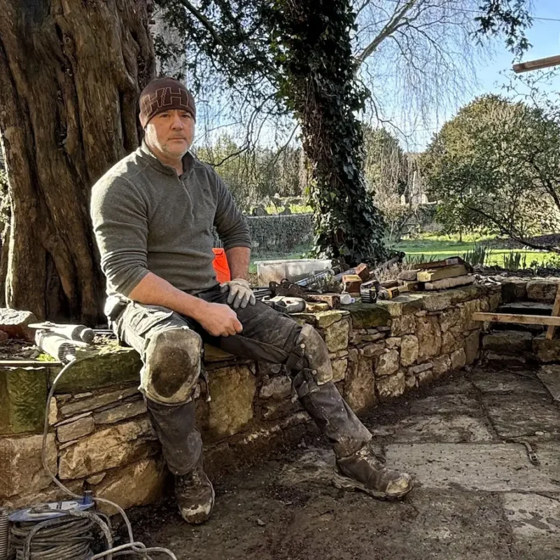 Simon, heritage stonemason and business owner in Shrewsbury, seated on stone wall